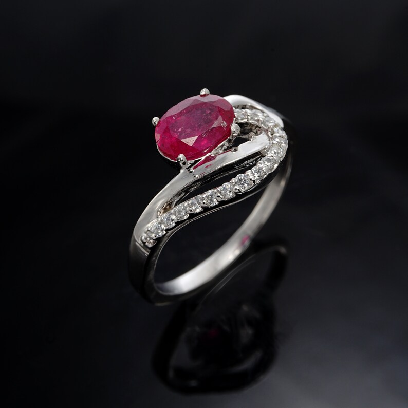 May include: A silver ring featuring a red ruby gemstone and a row of small diamonds set in the band.