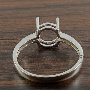 May include: Silver ring setting with a round bezel for a gemstone. The setting has a double prong design.
