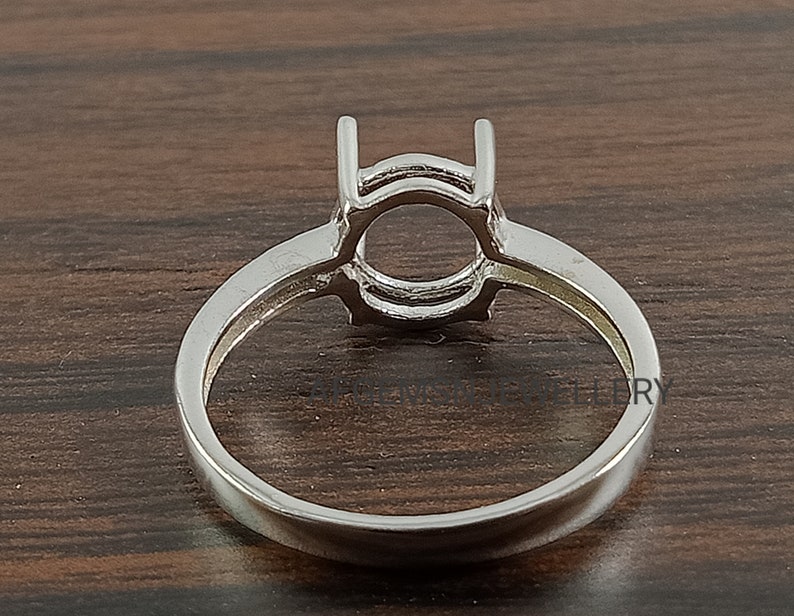 May include: Silver ring setting with a round bezel for a gemstone. The setting has a double prong design.