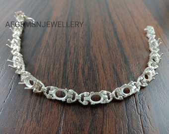 May include: Silver bracelet with oval-shaped settings for gemstones. The bracelet is made of a chain-link design with a polished finish.