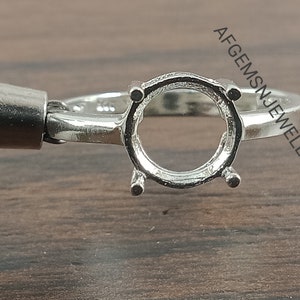 May include: Silver ring setting with a round bezel for a gemstone. The setting is designed to hold a round stone.