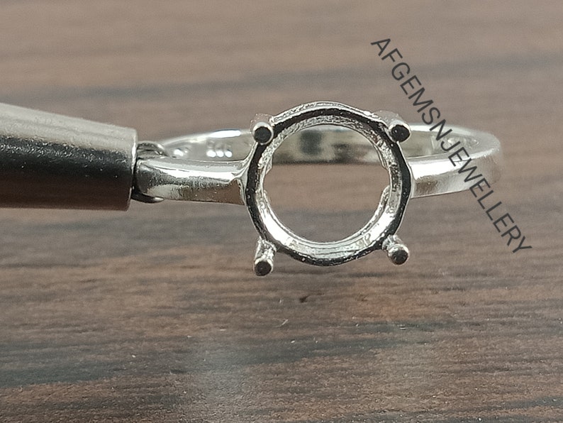 May include: Silver ring setting with a round bezel for a gemstone. The setting is designed to hold a round stone.