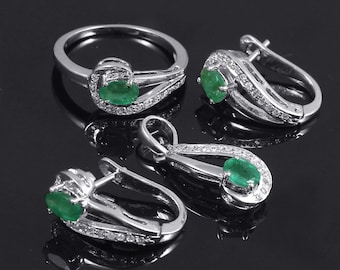 May include: A silver ring, pendant, and earrings set with green oval-shaped gemstones and clear round stones. The jewelry is on a black background.