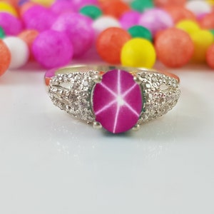 May include: A silver ring with a pink star sapphire gemstone surrounded by smaller white gemstones.