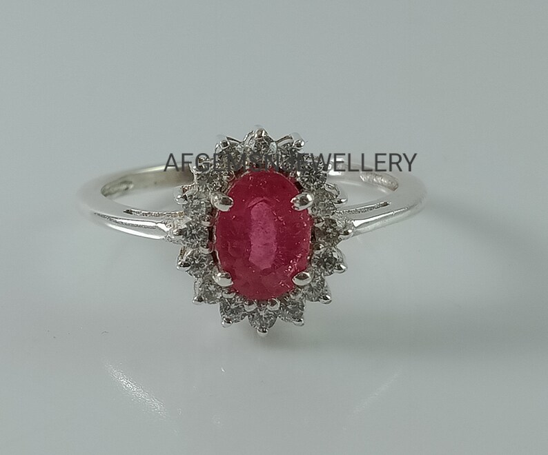 Pu&ograve; includere: Un anello d'argento con un grande rubino ovale circondato da pietre bianche pi&ugrave; piccole.