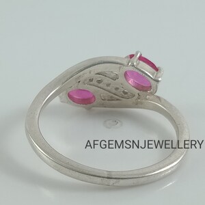 May include: A silver ring with two pink oval-shaped stones and a row of smaller stones. The ring is set on a white background. AFGEMSNJEWELLERY is printed on the ring.
