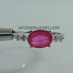 K&ouml;nnte beinhalten: Ein silberner Ring mit einem gro&szlig;en ovalen rosafarbenen Edelstein und zwei kleineren runden wei&szlig;en Edelsteinen auf jeder Seite. Der Ring liegt auf einem wei&szlig;en Hintergrund. Der Text 'AFGEMSNJEWELLERY' ist oben in der Mitte des Bildes zu sehen.