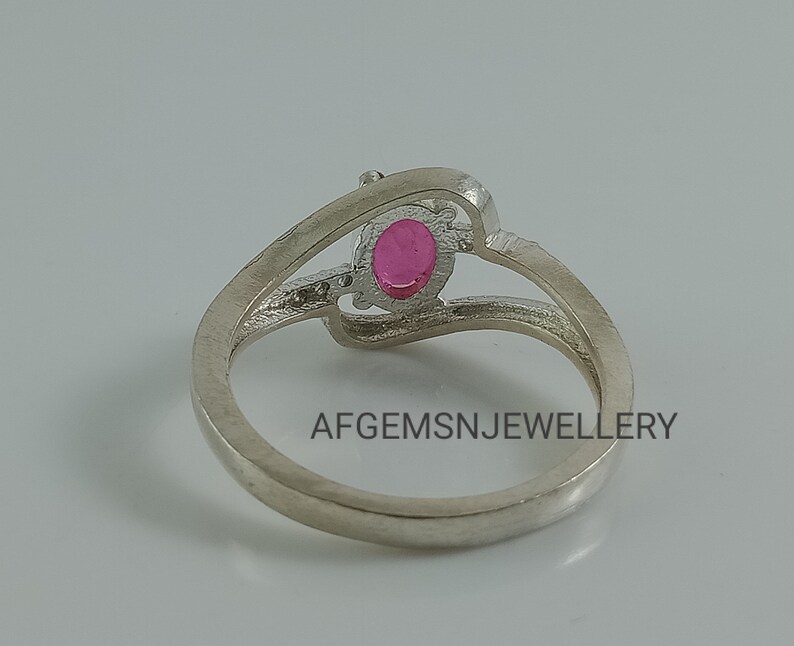 Puede incluir: Un anillo de plata con una piedra preciosa ovalada rosa engastada en una banda delicada y retorcida. El anillo est&aacute; dise&ntilde;ado con un patr&oacute;n &uacute;nico e intrincado. AFGEMSNJEWELLERY est&aacute; impreso en la banda.