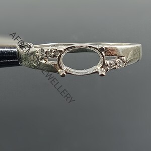 Op de afbeelding: Zilveren ringbezetting met een ovale bezel en kleine heldere stenen op de band.
