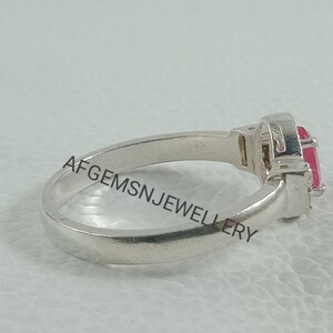 K&ouml;nnte beinhalten: Ein silberner Ring mit einem rosafarbenen Edelstein, der in einer Krappenfassung sitzt. Der Ring liegt auf einer wei&szlig;en Oberfl&auml;che.