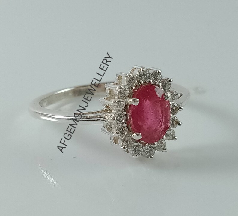 Pu&ograve; includere: Un anello d'argento con un grande rubino ovale circondato da pietre bianche pi&ugrave; piccole.