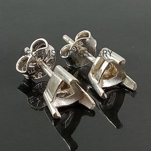 May include: A pair of silver earring settings with a triangular shaped bezel. The settings are marked with "925" on the back.