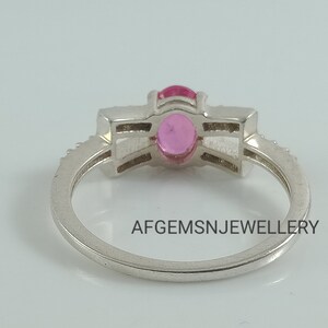May include: A silver ring with a pink gemstone set in a prong setting. The ring has a band of small diamonds.