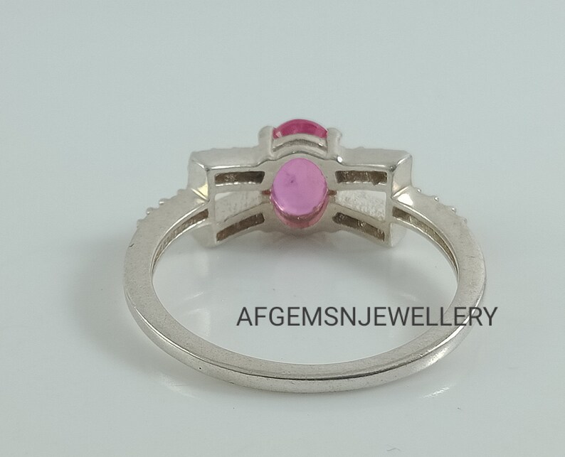 May include: A silver ring with a pink gemstone set in a prong setting. The ring has a band of small diamonds.