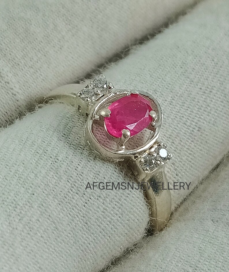 K&ouml;nnte beinhalten: Ein silberner Ring mit einem rosafarbenen ovalen Edelstein, der von kleineren wei&szlig;en Edelsteinen umgeben ist. Der Ring ist in einem filigranen, durchbrochenen Design gefasst.