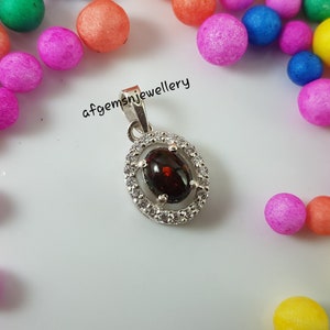 May include: A silver pendant with a red opal gemstone surrounded by a halo of small white cubic zirconia stones. The pendant is on a white background.