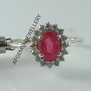 Pu&ograve; includere: Un anello d'argento con un grande rubino ovale circondato da un'aureola di diamanti pi&ugrave; piccoli.