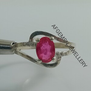 Puede incluir: Un anillo de plata con una piedra ovalada rosa engastada en una banda delicada y retorcida. El anillo est&aacute; adornado con peque&ntilde;as piedras transparentes.