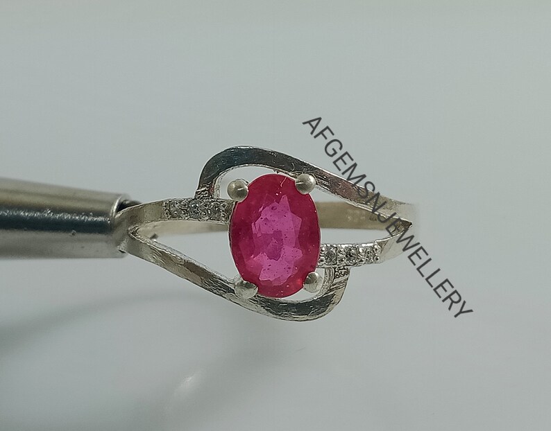 Puede incluir: Un anillo de plata con una piedra ovalada rosa engastada en una banda delicada y retorcida. El anillo est&aacute; adornado con peque&ntilde;as piedras transparentes.