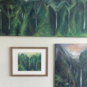 May include: Three framed paintings of a lush green landscape with waterfalls. The paintings are in different sizes and are hung on a white wall.