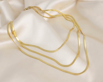 May include: A gold chain necklace with three strands of a snake chain design.