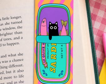 May include: A rectangular bookmark with an orange background featuring vertical pink wavy lines. The center displays a teal sardine tin illustration containing two pink fish and a black cat with white eyes. The text reads SARDI IN OLIVE OIL.
