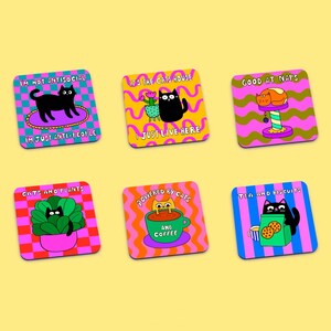 May include: Set of six colorful square coasters featuring black cats and humorous cat-themed sayings. The coasters have a variety of patterns, including checkered, wavy, and striped designs. The sayings on the coasters include "I'm not antisocial, I'm just anti-people", "It's the cats house, I just live here", "Good at naps", "Cats and plants", "Powered by cats and coffee", and "Tea and biscuits".