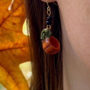 May include: Gold pumpkin earrings with black beads and a green stem. The pumpkin is orange and has a hollowed-out center.