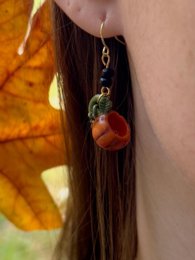 May include: Gold pumpkin earrings with black beads and a green stem. The pumpkin is orange and has a hollowed-out center.
