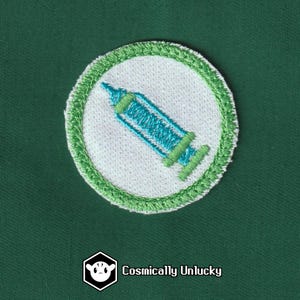 May include: A white embroidered patch with a green border, featuring a blue and green syringe.
