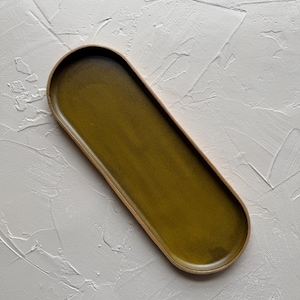 May include: An olive green ceramic serving tray with a rounded rectangular shape. The tray has a light brown rim and a smooth, glossy surface. The tray is approximately 12 inches long and 5 inches wide.