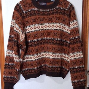 May include: A brown and cream-colored sweater with a geometric pattern. The sweater features a crew neck, long sleeves, and a ribbed hem and cuffs. The pattern includes diamond and snowflake-like shapes.