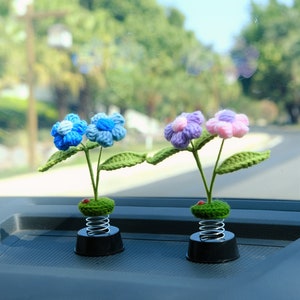 May include: Two crocheted flower car decorations with spring bases. One decoration has blue flowers and the other has purple and pink flowers.