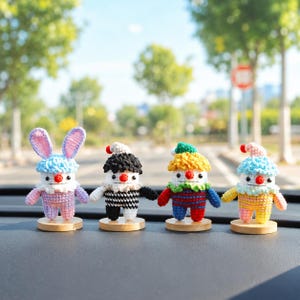 May include: Four colorful, handmade crochet figures with round wooden bases. The figures include a bunny with blue ears, a clown with a black and white outfit, and two other clowns with different colored outfits. Each figure has a red nose and a small hat.