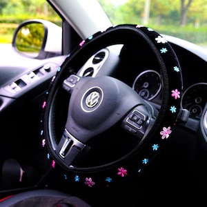 May include: Black steering wheel cover with pink and blue flower embroidery. The cover is made of soft, plush material and is designed to fit most standard steering wheels.