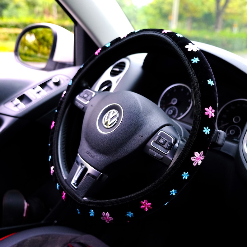 May include: Black steering wheel cover with pink and blue flower embroidery. The cover is made of soft, plush material and is designed to fit most standard steering wheels.