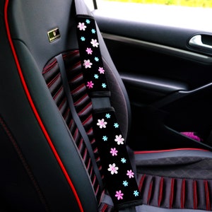 May include: Black car seat with red stitching and a black seatbelt cover with pink and blue floral embroidery.