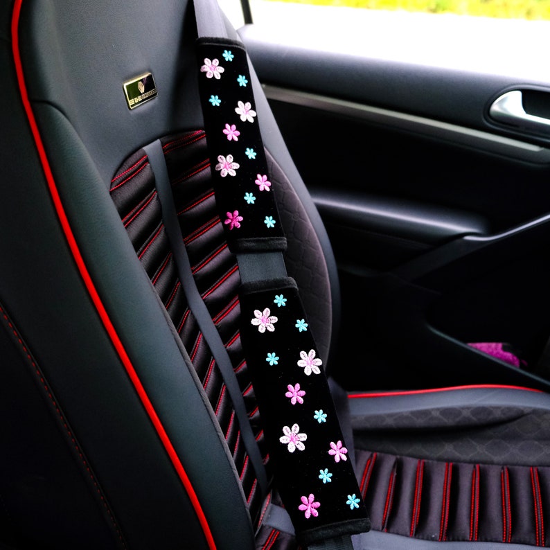May include: Black car seat with red stitching and a black seatbelt cover with pink and blue floral embroidery.