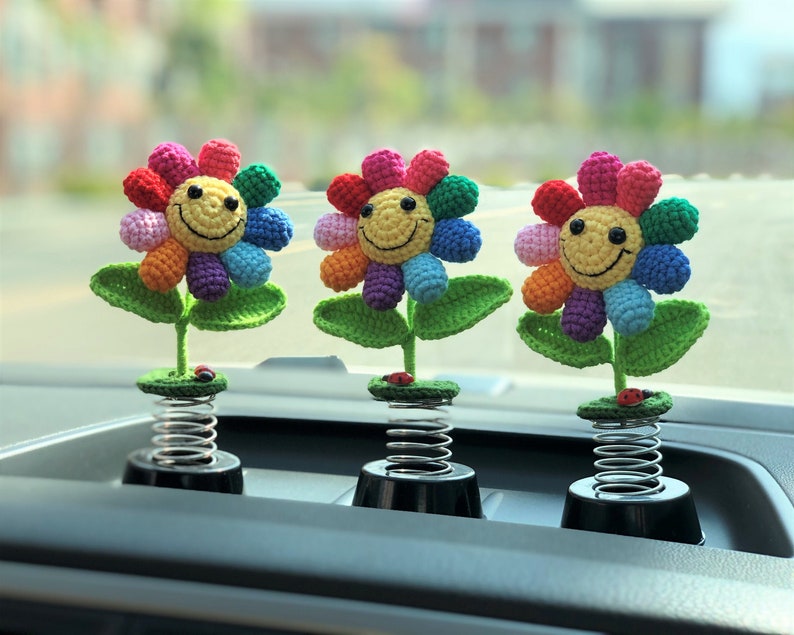 May include: Three colorful crocheted flowers with smiling faces on spring-loaded bases. The flowers are rainbow colored and have green leaves. The bases are black and silver.