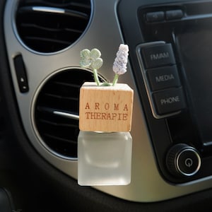 Può includere: Un profumatore per auto in legno con la scritta "Aroma Therapie" e un piccolo arrangiamento di fiori all'uncinetto.