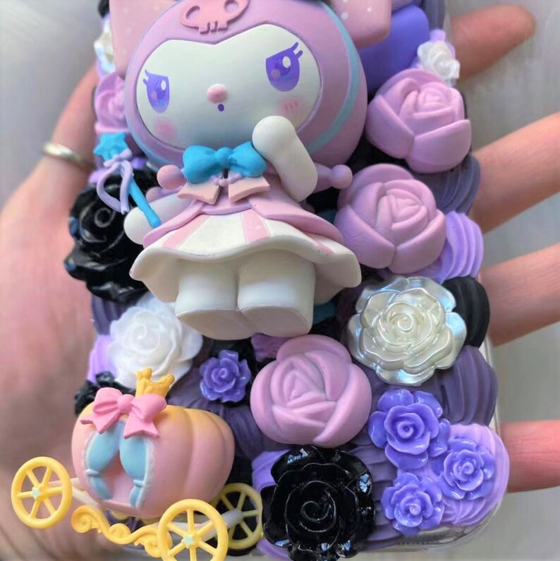 Puede incluir: Una funda de tel&eacute;fono rosa y morada decorada con un personaje en 3D, flores y un carruaje. El personaje es un conejo blanco con un vestido rosa y un lazo azul. Las flores son en tonos de rosa, morado y negro. El carruaje es dorado y rosa.