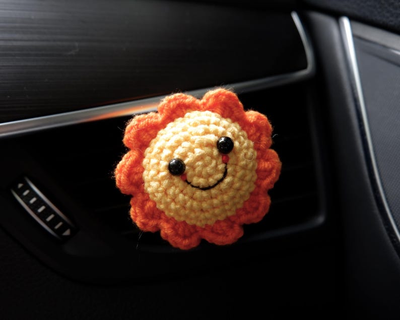Puede incluir: Un clip de ventilaci&oacute;n de coche con forma de sol tejido a ganchillo. El sol tiene un centro amarillo con un borde naranja con volantes. Cuenta con ojos de bot&oacute;n negros y una sonrisa cosida. El clip est&aacute; dise&ntilde;ado para sujetarse a una rejilla de ventilaci&oacute;n del coche.