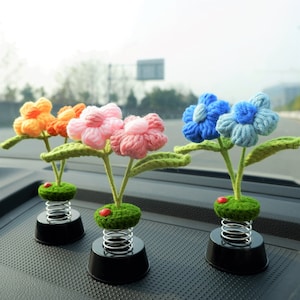 May include: Four colorful crocheted flower car air fresheners with spring bases. The flowers are pink, blue, orange, and yellow.
