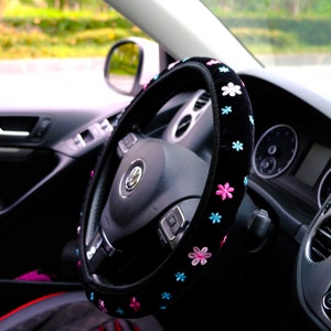 May include: Black steering wheel cover with pink and blue embroidered flowers. The cover is made of soft, plush material and is designed to fit most standard steering wheels.