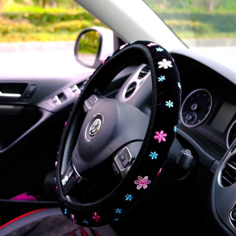 May include: Black steering wheel cover with pink and blue embroidered flowers. The cover is made of soft, plush material and is designed to fit most standard steering wheels.