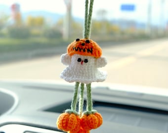 May include: A white crocheted ghost wearing an orange and black pumpkin hat with the word "WYN" on it. The ghost has green yarn legs and is holding two orange crocheted pumpkins.