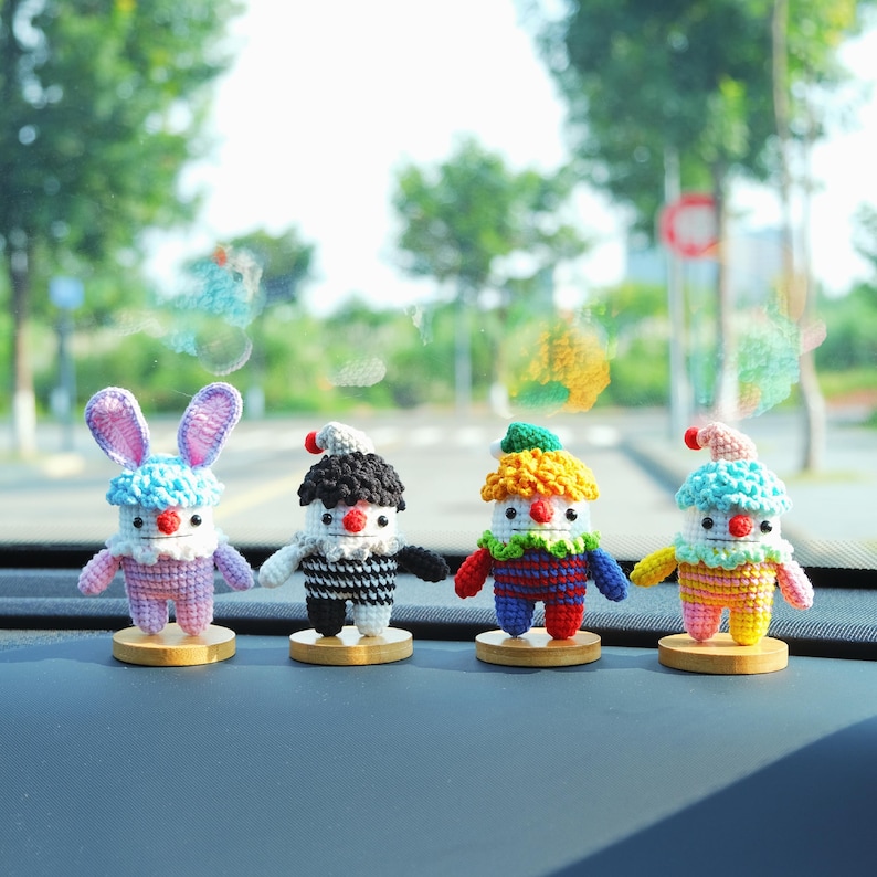 May include: Four colorful, handmade crochet figures. One is a bunny with blue ears, the others are clown-like with different colored hats and outfits. Each figure is mounted on a small wooden base, creating a whimsical display.