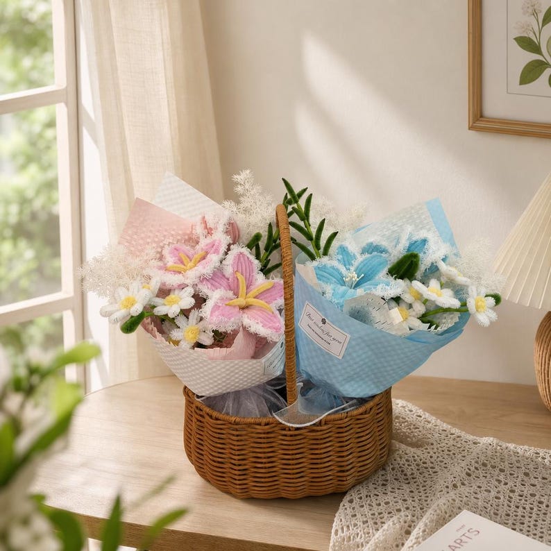 May include: A woven basket holds two bouquets of handmade flowers. One bouquet features pink and white lilies and daisies, wrapped in pink paper. The other bouquet has blue lilies and white daisies, wrapped in blue paper. The basket sits on a wooden surface.