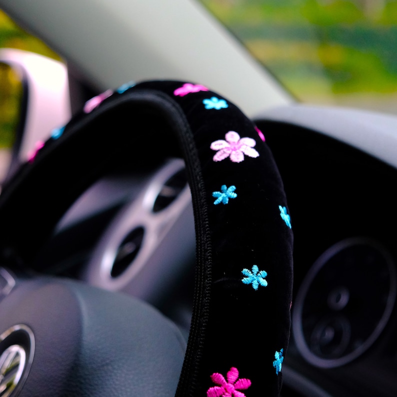 May include: Black steering wheel cover with pink and blue embroidered flowers.
