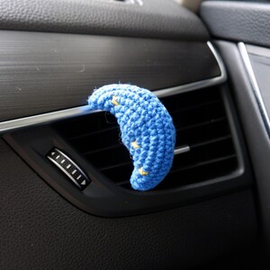 Puede incluir: Un difusor de ventilaci&oacute;n de coche con forma de media luna azul de ganchillo con detalles de estrellas amarillas. El accesorio hecho a mano se coloca en la ventilaci&oacute;n del coche, a&ntilde;adiendo un toque decorativo al interior del veh&iacute;culo.